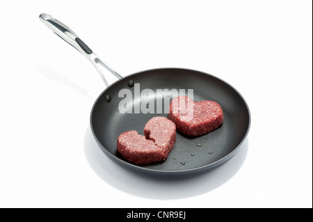 Two heart shaped beef burgers in a frying pan Stock Photo