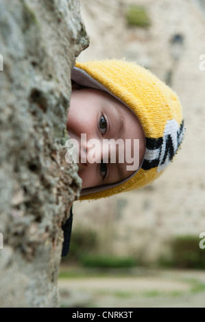 Boy peeking from behind tree Stock Photo