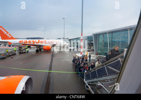 Amsterdam Schiphol Airport People boarding EasyJet plane airplane aeroplane mobile staircase stairs in winter. H Pier Stock Photo