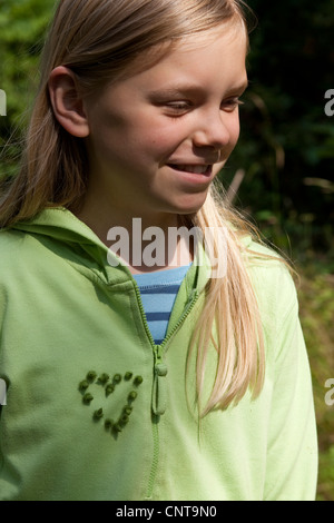common burdock, lesser burdock (Arctium minus), girl having fixed burr fruits at her pullover in the shape of a heart, Germany Stock Photo