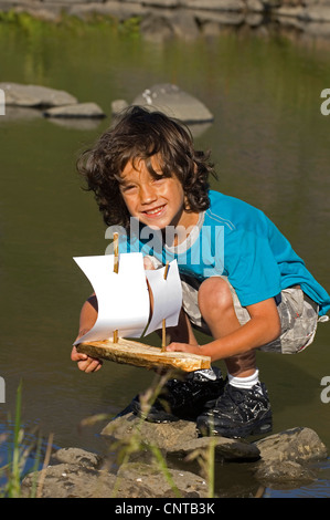 boy happily smiling while launching his self-made toy boat, France Stock Photo