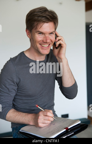 Smiling man on cell phone taking notes Stock Photo