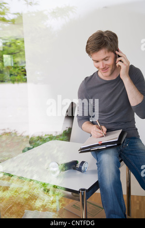 Man on cell phone taking notes Stock Photo