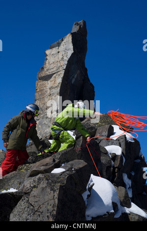 two ski alpinists with helmets and ski goggles climbing in the mountains, throwing the rope, France, Alps Stock Photo