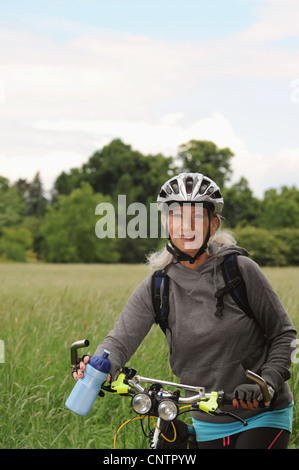 Older woman riding bicycle on rural road Stock Photo