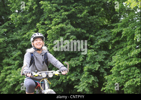 Older woman riding bicycle on rural road Stock Photo