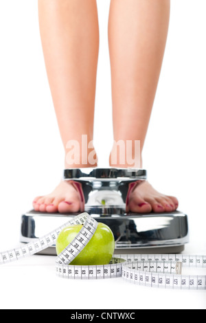 Diet and weight, young woman standing on a scale, only feet to be seen, a apple and a measuring tape Stock Photo