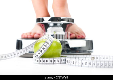 Diet and weight, young woman standing on a scale, only feet to be seen, a apple and a measuring tape Stock Photo
