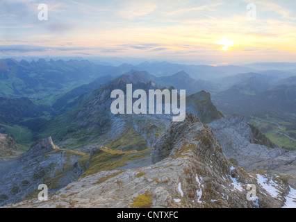 alpine ragged sharp karst mountain top ranges disapear in misty distance and green meadow at sunset, Switzerland Stock Photo