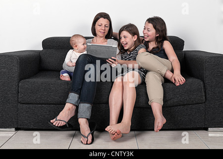 Mother with Three Daughters on Sofa with Tablet Computer Stock Photo