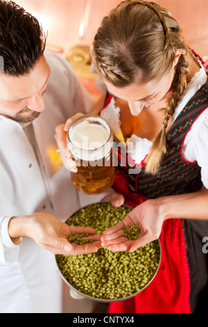 Woman in Tracht and brewer with beer stein and hops in her brewery Stock Photo