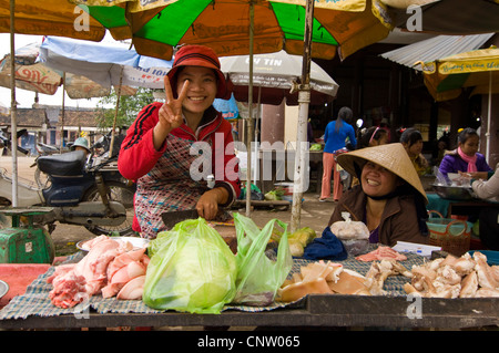 Horizontal portrait two women at a stall selling chunks of meat in a traditional wet market in a rural village in Vietnam. Stock Photo