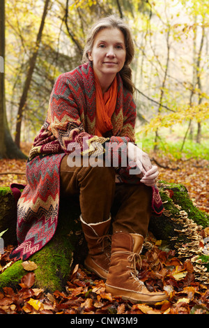 Older woman sitting on stump in forest Stock Photo