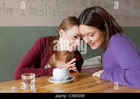 Women whispering to each other in cafe Stock Photo