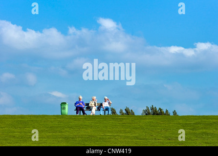 three white-haired women sitting on a bench on an dyke at the North Sea in Dorum-Neufeld, Germany, Lower Saxony Stock Photo