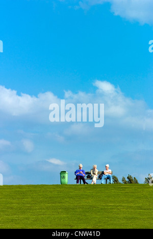 three white-haired women sitting on a bench on an dyke at the North Sea in Dorum-Neufeld, Germany, Lower Saxony Stock Photo