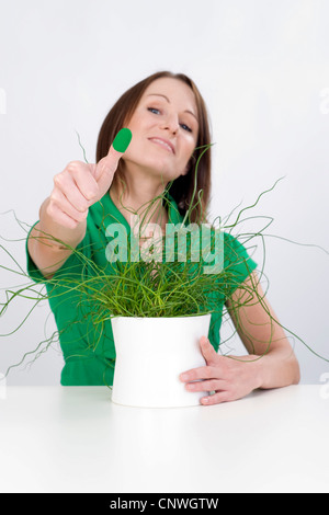 Lesser Corkscrew Rush, Corkscrew Rush (Juncus effusus Spiralis, Juncus effusus 'Spiralis', Juncus effusus f. spiralis, Juncus spiralis), young woman with potted plant, presenting a green thumb Stock Photo