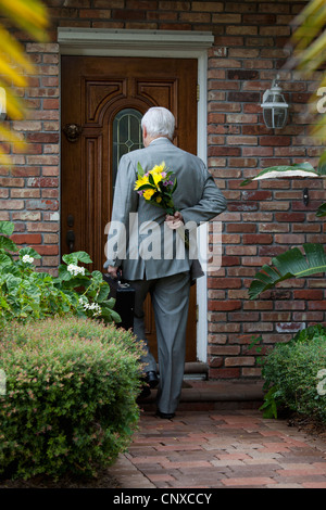 A businessman carrying flowers behind his back, arriving home Stock Photo