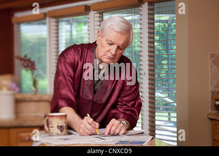 A senior man in a silk robe writing on a newspaper Stock Photo
