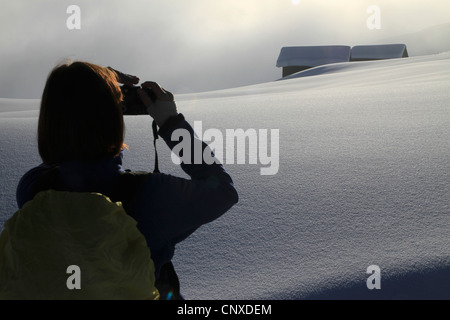 Hiker takes photograph of snowy log cabins in the distance Stock Photo