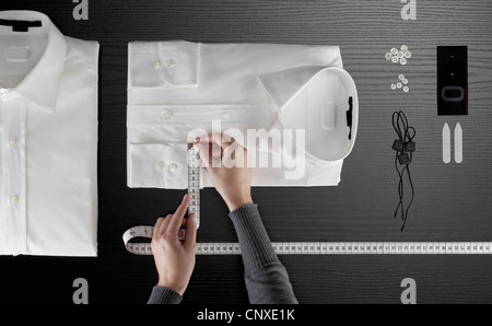 A tailor measuring a button down shirt, focus on hands Stock Photo