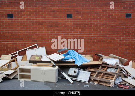 Broken furniture and scraps of garbage piled up against a brick wall Stock Photo