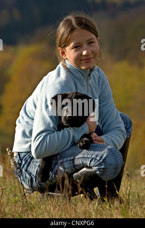 Labrador Retriever (Canis lupus f. familiaris), girl crouching in a meadow and holding a puppy Stock Photo
