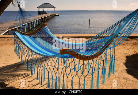 view from the sand beach over a hamock at a wooden footbridge leading into the sea, Belize, Ambergris Caye Stock Photo