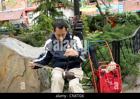 An Asian man busker playing an erhu, the two-string Chinese fiddle. Stock Photo