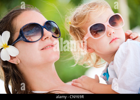 frangipani plant, nosegaytree (Plumeria alba), young mother with frangipani blossom in the hair and little daughter in the arms cuddling up to her Stock Photo