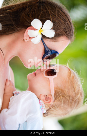 frangipani plant, nosegaytree (Plumeria alba), young mother with frangipani blossom in the hair and little daughter in the arms cuddling up to her Stock Photo