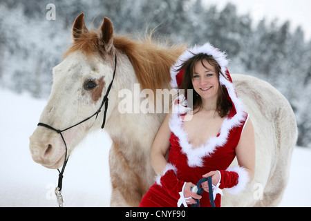 young woman in a revealing Santa costume leaning against a white horse in a winter landscape Stock Photo