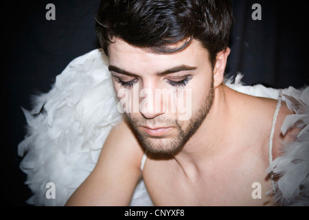 Sad young man with black streaked eye makeup, wearing angel's wings Stock Photo