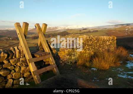 A ladder stile over a drystone wall near Glossop, Peak District, Derbyshire, England, UK. Snow covered Bleaklow in the distance. Stock Photo