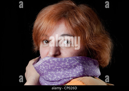 Middle aged woman hiding behind scarf looking surprised Stock Photo