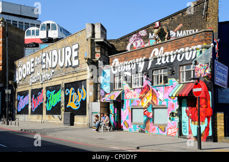 Recycled tube train carriages used as artists studios perched above old railway viaduct walls below arty graffiti in Shoreditch East London England UK Stock Photo