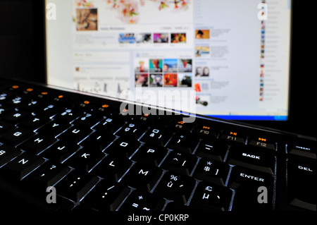 Black computer keyboard with illuminated backlit white characters on keys and pc screen in the dark Stock Photo