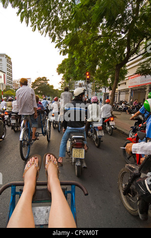 Vertical view of a Western tourist on a cycle rickshaw travelling through traffic on the crazy streets of Ho Chi Minh City. Stock Photo