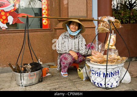 Horizontal portrait of a Saigonese street vendor making hot waffles from her yoke to sell sitting on the pavement in Ho Chi Minh, Vietnam. Stock Photo