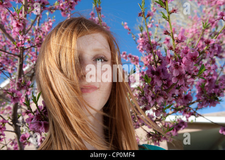 Spring, teenage girl smiling at camera with cherry blossoms and blue sky.