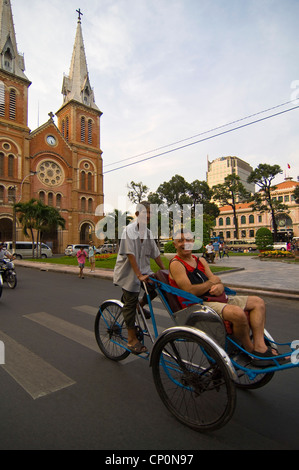 Vertical view of a cycle rickshaw with Western tourist & Saigon Notre-Dame Basilica, Nhà thờ Đức Bà Sài Gòn in Ho Chi Minh City Stock Photo