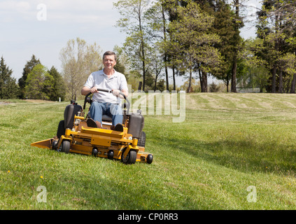 Senior retired male mowing the lawn and cutting the grass on a large lawn using yellow zero-turn ride on lawnmower Stock Photo