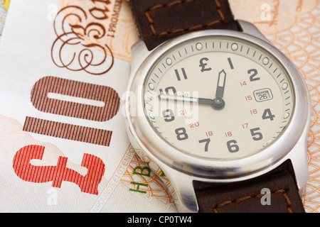 Wristwatch clock on a Sterling ten pound note GBP to illustrate time to put money in a pension concept. England, UK, Britain Stock Photo