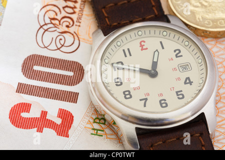 Wristwatch clock on a Sterling ten pound note and a pound coin to illustrate financial concept time is money in business. England UK Britain Stock Photo