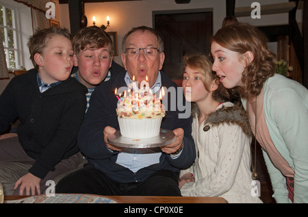 Grandchildren blowing out the candles on their Grandfather's birthday cake Stock Photo