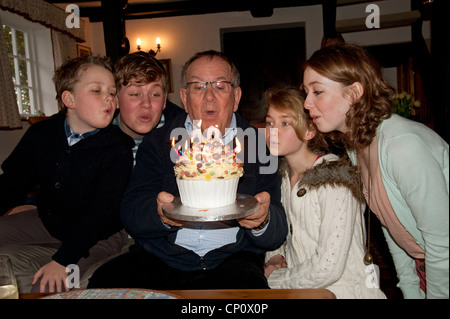 Grandchildren blowing out the candles on their Grandfather's birthday cake Stock Photo