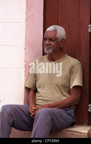 Daily life in Cuba - Afro-Caribbean man sat on steps in doorway at Trinidad, Cuba Stock Photo