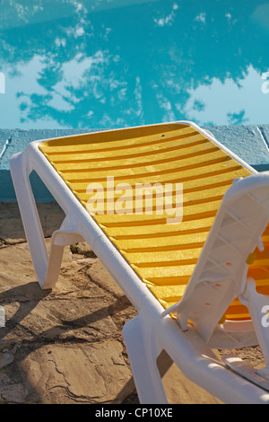 yellow sun lounger by side of swimming pool early in the morning with water droplets on, condensation at Trinidad, Cuba in March Stock Photo