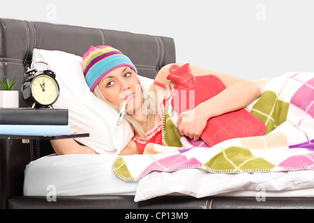 Ill woman in a bed holding a hot-water bottle and a thermometer in her mouth Stock Photo