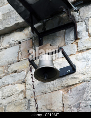 it's a photo of a big bell hanged against the wall in a school or stone wall. There is a chain to make it bells. It's in copper